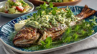 photo of a platter with a roasted whole carp coated with a creamy butter shredded endive leaf sauce